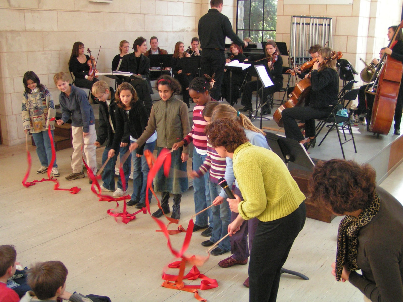 Kinder tanzen mit roten Bändern vor einem Orchester