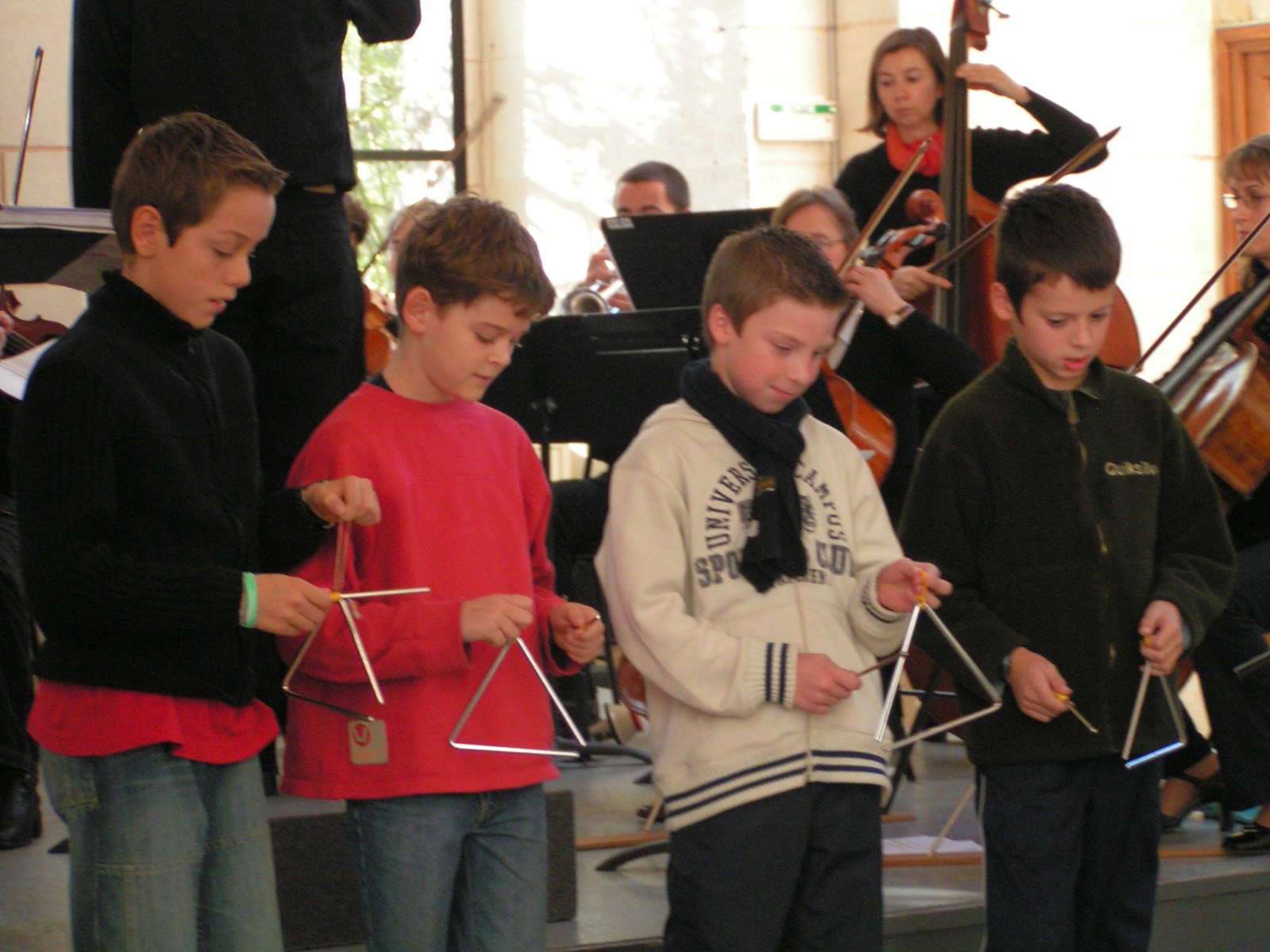 Kinder spielen Triangel vor einem Orchester