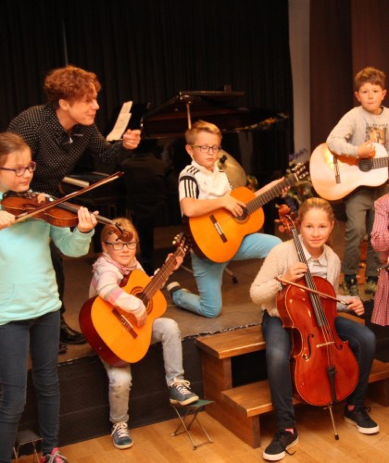 Kinder spielen Geige, Gitarre und Cello auf der Bühne